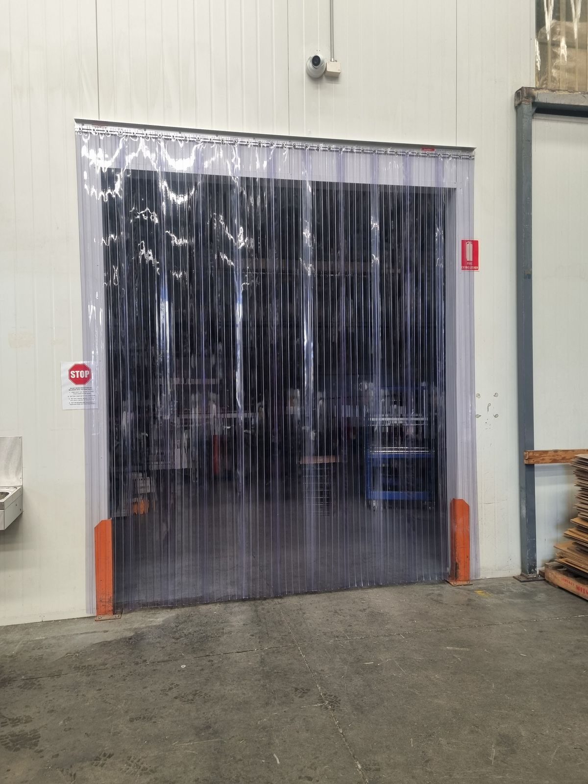 Clear PVC strip curtain on a wide internal doorway with orange bollard protection