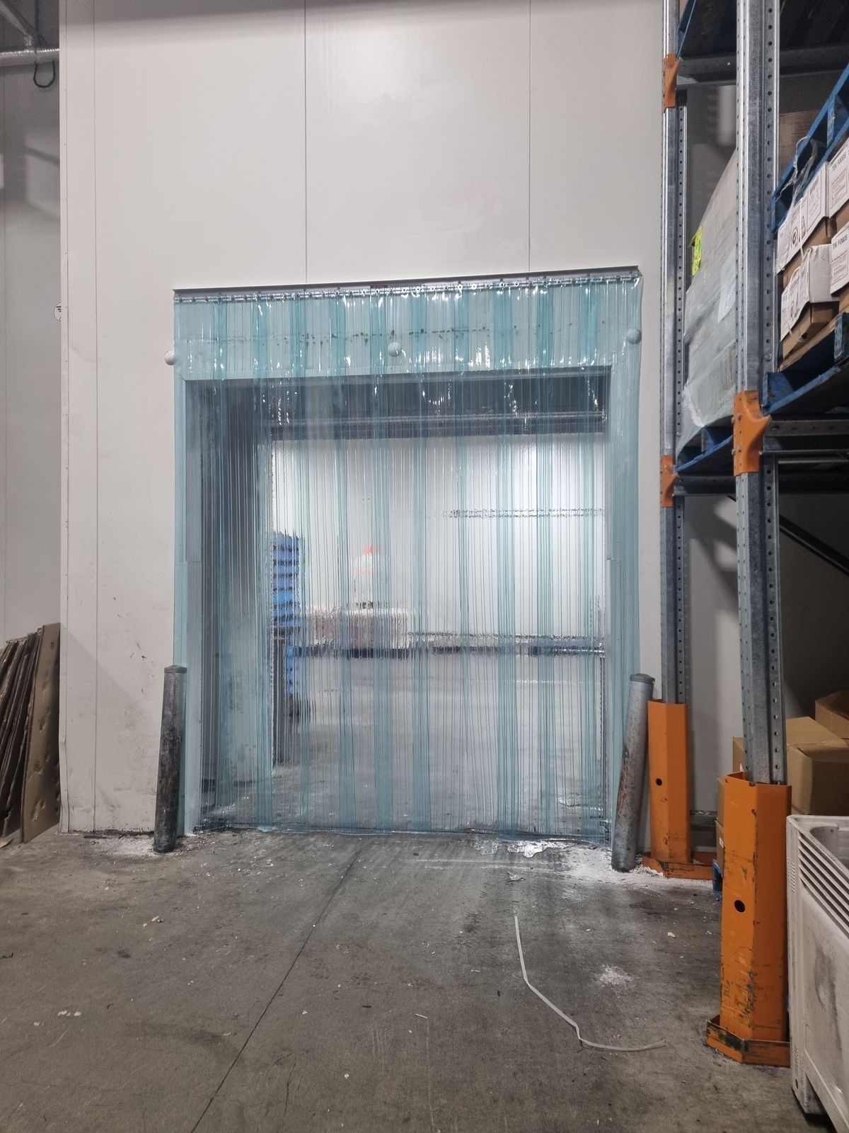Clear PVC strip curtain on a loading dock doorway beside pallet racking