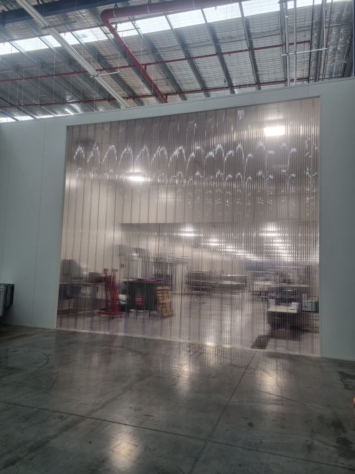 Clear PVC strip curtain partition across a food production area, seen from an angle