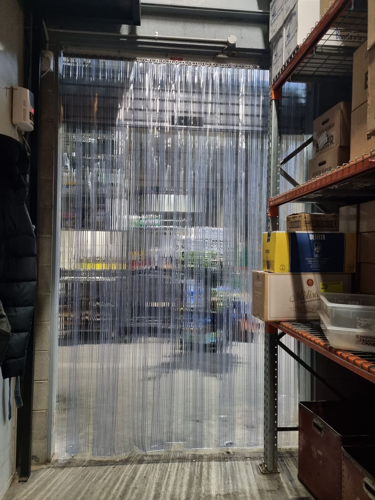 Clear PVC strip curtain on a parts store doorway beside workshop racking