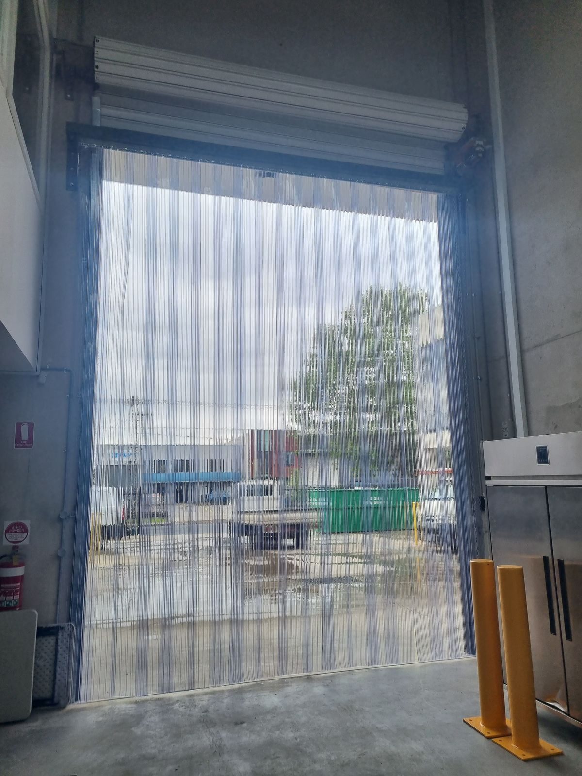 Clear PVC strip door on a wide vehicle doorway opening onto a hardstand