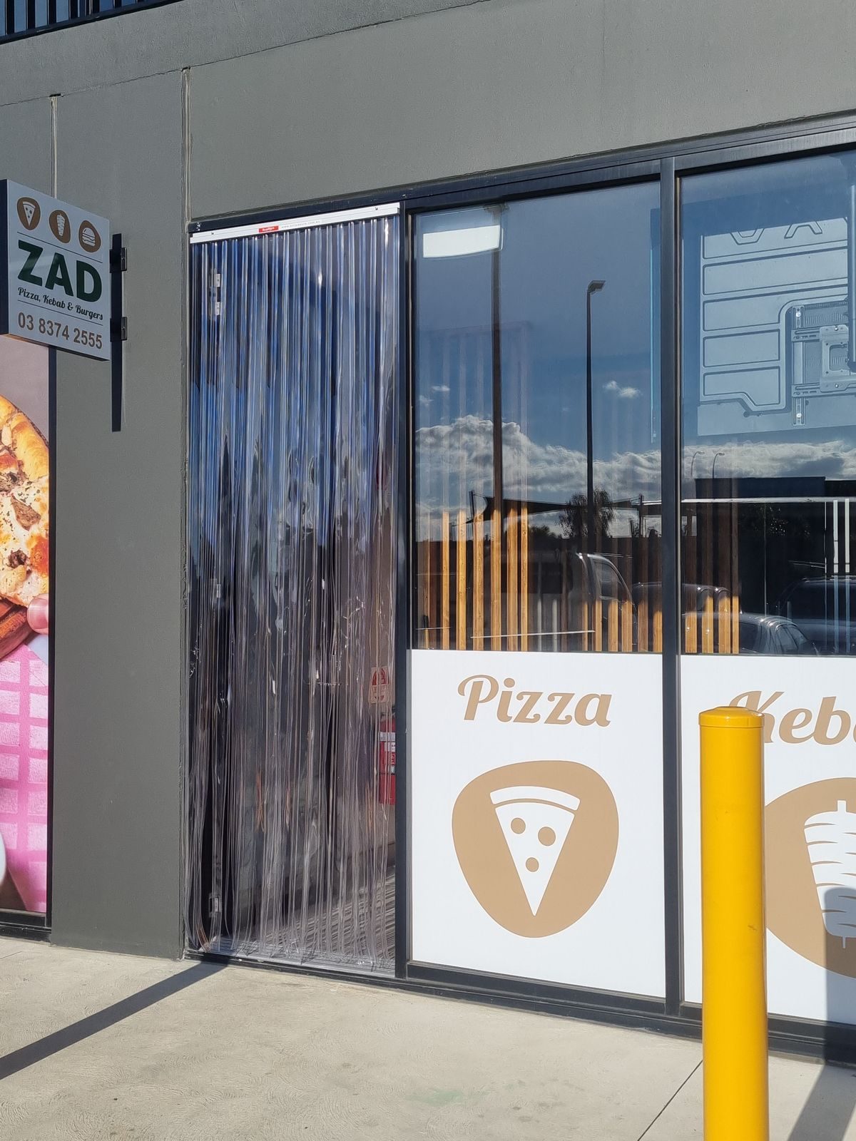 Clear PVC strip curtain on the front door of a pizza and kebab shop
